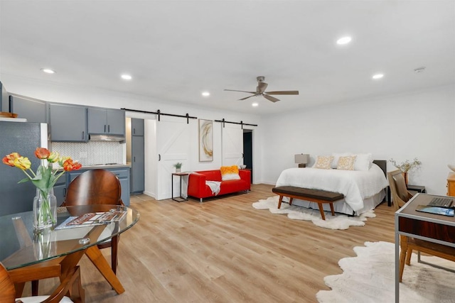 bedroom with light hardwood / wood-style flooring, stainless steel refrigerator, a barn door, and ceiling fan