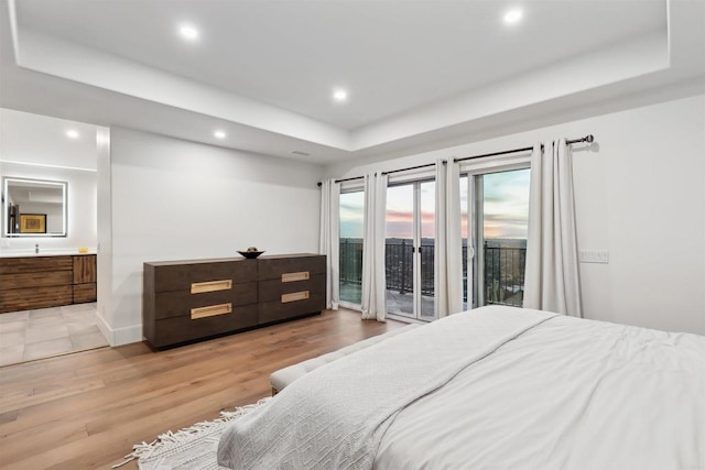 bedroom featuring access to exterior, a tray ceiling, ensuite bath, and light wood-type flooring