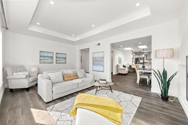 living room with dark wood-type flooring and a tray ceiling