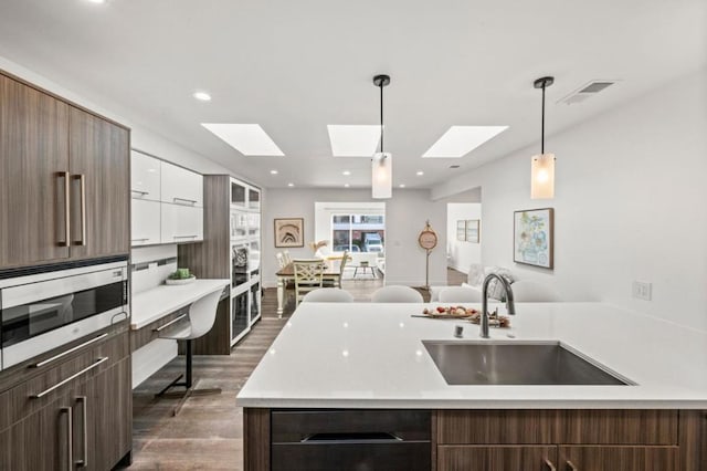 kitchen with sink, white cabinetry, hanging light fixtures, stainless steel microwave, and a kitchen island with sink