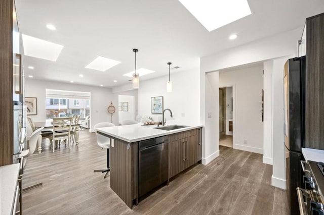 kitchen with a skylight, sink, a kitchen island with sink, stainless steel appliances, and dark brown cabinets