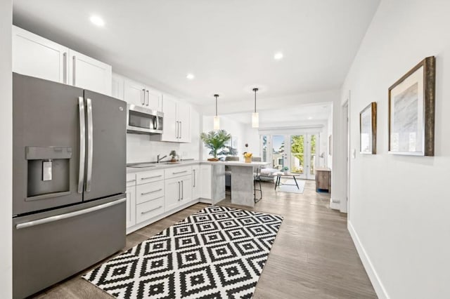 kitchen with stainless steel appliances, light hardwood / wood-style floors, white cabinets, decorative light fixtures, and kitchen peninsula