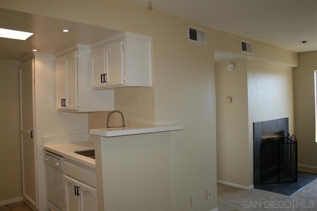 kitchen featuring white dishwasher, a tile fireplace, and white cabinets