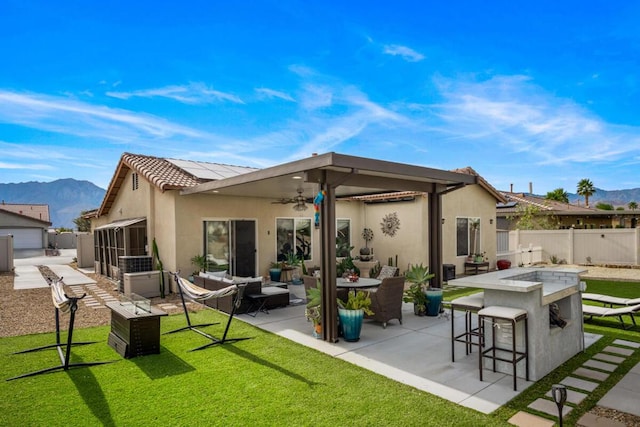 back of property with a lawn, exterior bar, ceiling fan, a mountain view, and a patio area