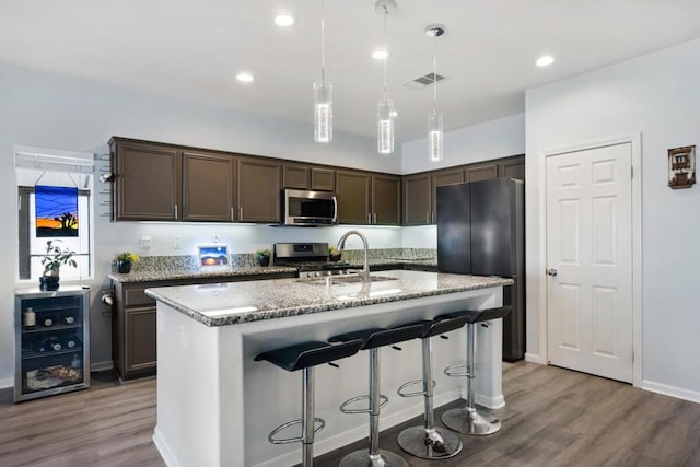 kitchen with pendant lighting, sink, hardwood / wood-style floors, stainless steel appliances, and an island with sink