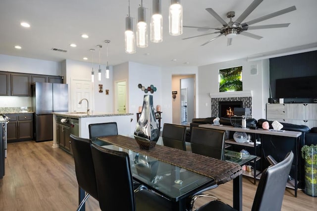 dining area with a fireplace, light hardwood / wood-style flooring, sink, and ceiling fan