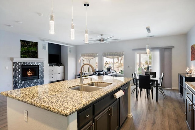 kitchen featuring a kitchen island with sink, sink, decorative light fixtures, and light stone countertops