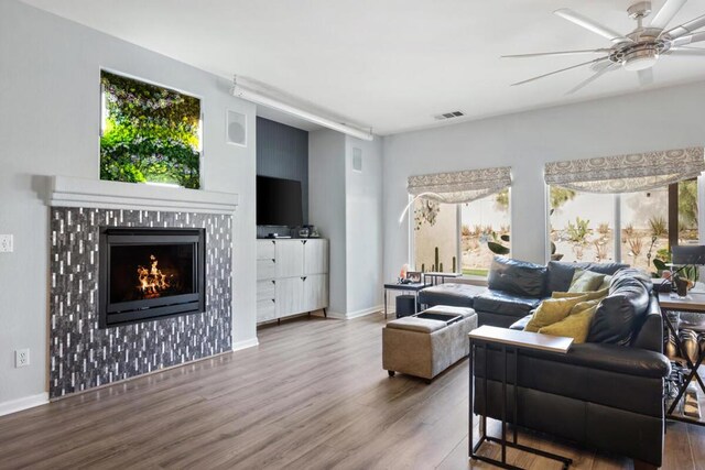 living room featuring a tiled fireplace, wood-type flooring, and ceiling fan