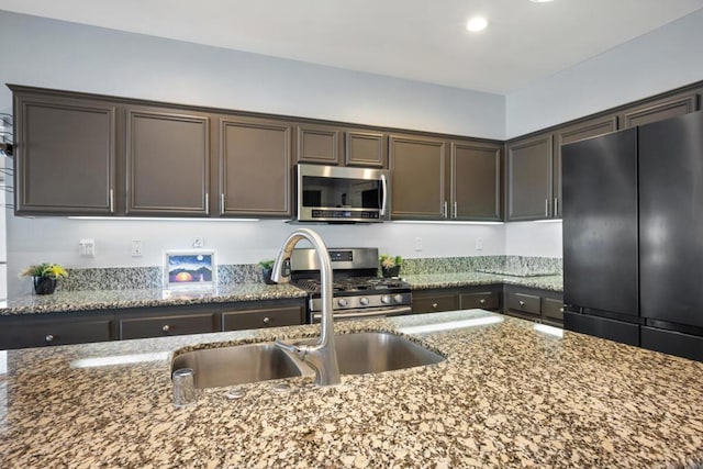 kitchen with light stone counters, dark brown cabinetry, stainless steel appliances, and sink