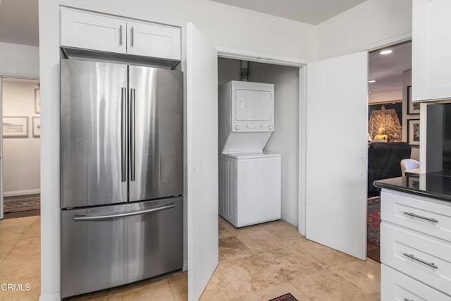 kitchen with stacked washing maching and dryer, white cabinets, and stainless steel refrigerator