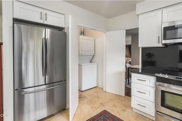 kitchen with stainless steel appliances, stacked washer and dryer, white cabinets, and dark countertops