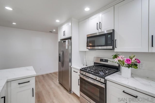 kitchen with appliances with stainless steel finishes, white cabinets, light stone counters, and light hardwood / wood-style flooring