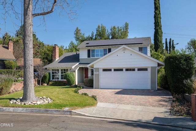 view of front of property featuring a garage, a front lawn, and solar panels