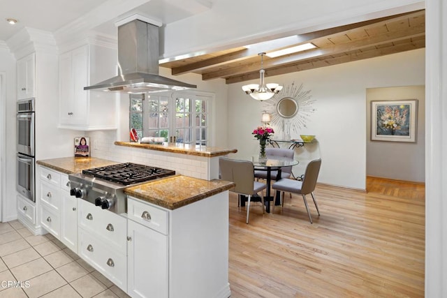 kitchen with island range hood, dark stone counters, beamed ceiling, stainless steel appliances, and white cabinets