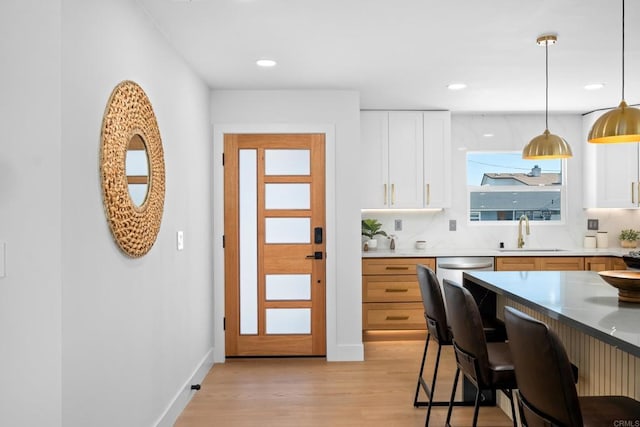 kitchen with sink, hanging light fixtures, light hardwood / wood-style floors, white cabinets, and decorative backsplash