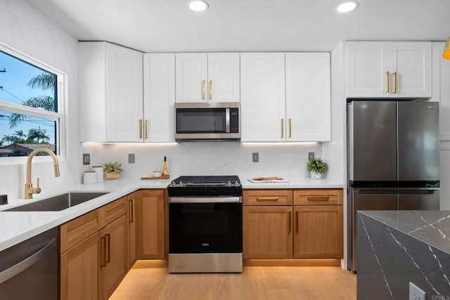 kitchen with sink, white cabinetry, light stone counters, light wood-type flooring, and stainless steel appliances