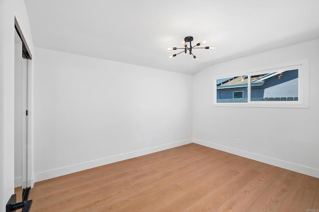 empty room with vaulted ceiling, a chandelier, and light hardwood / wood-style flooring