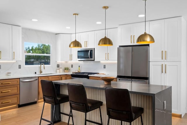 kitchen featuring sink, appliances with stainless steel finishes, white cabinetry, hanging light fixtures, and light hardwood / wood-style floors