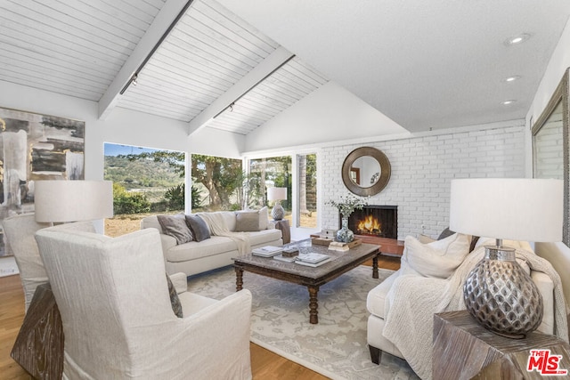 living room featuring a brick fireplace, vaulted ceiling with beams, and light hardwood / wood-style floors