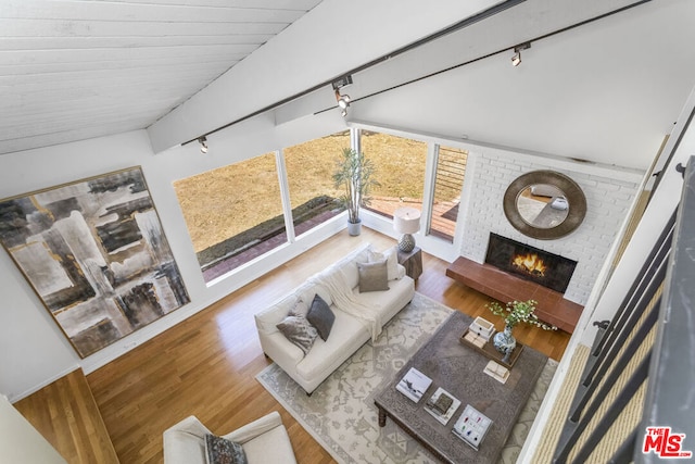 living room with wood-type flooring, vaulted ceiling, track lighting, and a fireplace