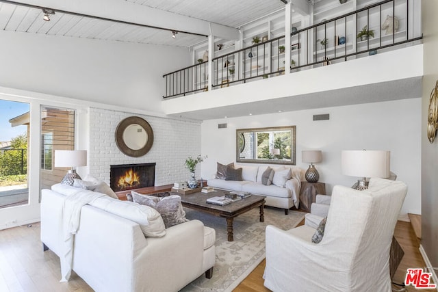 living room featuring wood ceiling, light hardwood / wood-style flooring, a high ceiling, a brick fireplace, and beamed ceiling