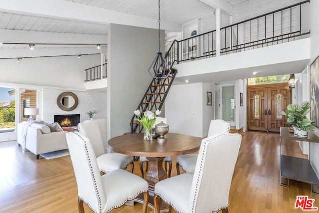 dining space featuring a brick fireplace, wooden ceiling, hardwood / wood-style flooring, beam ceiling, and a high ceiling