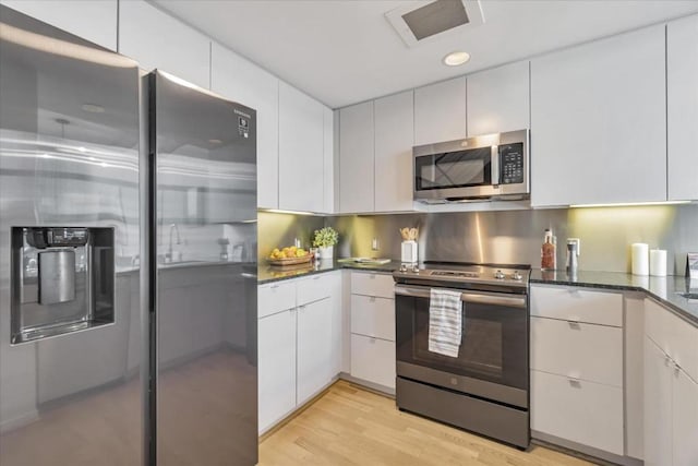 kitchen with dark stone countertops, light wood-type flooring, white cabinets, and appliances with stainless steel finishes