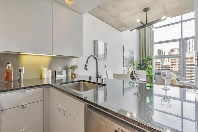 kitchen featuring sink, hanging light fixtures, dark stone counters, and white cabinets