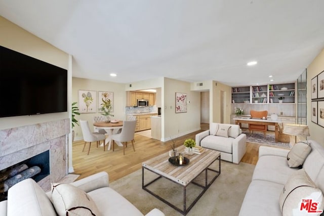 living room with a high end fireplace and light wood-type flooring