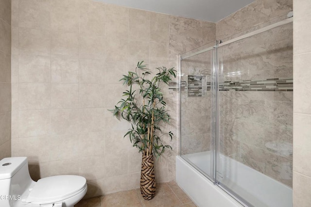 bathroom with tile walls, tile patterned flooring, shower / bath combination with glass door, and toilet