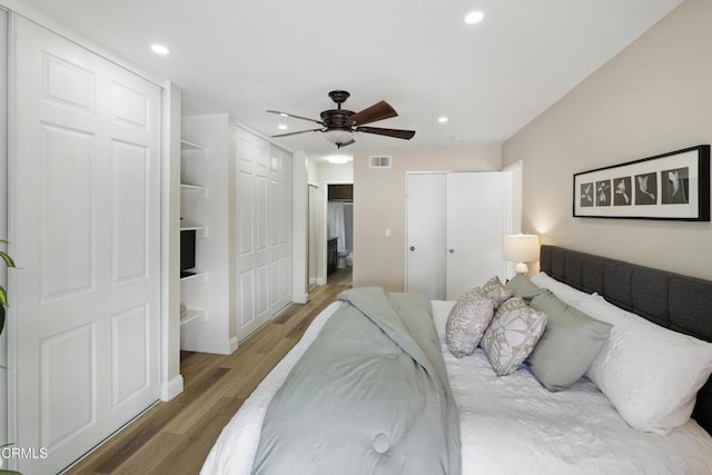 bedroom featuring ceiling fan, wood-type flooring, and two closets