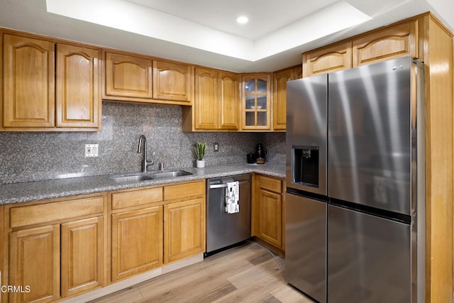 kitchen featuring sink, stainless steel appliances, light hardwood / wood-style floors, light stone countertops, and a raised ceiling