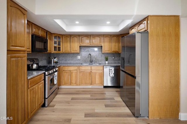 kitchen with stainless steel appliances, a raised ceiling, sink, and dark stone counters