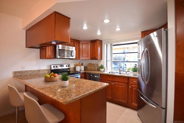 kitchen with sink, appliances with stainless steel finishes, light stone countertops, a kitchen bar, and kitchen peninsula