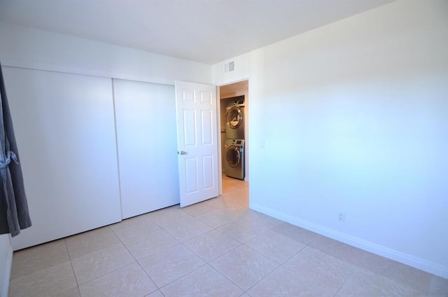 unfurnished bedroom featuring stacked washer and clothes dryer, light tile patterned floors, and a closet