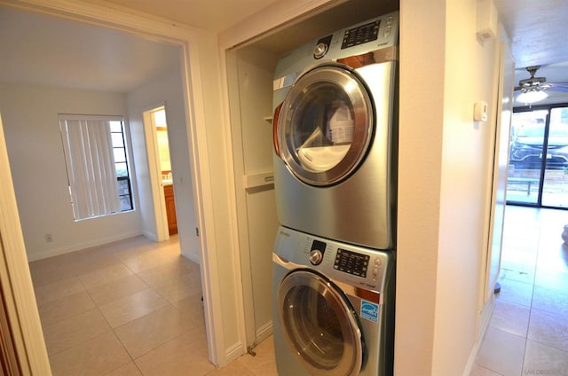 clothes washing area featuring stacked washer / dryer, light tile patterned flooring, and ceiling fan