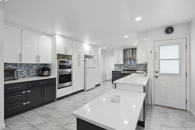 kitchen featuring wall chimney exhaust hood, sink, white fridge, stainless steel double oven, and white cabinets