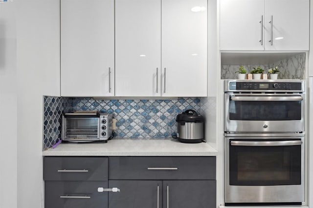 kitchen featuring tasteful backsplash, stainless steel double oven, gray cabinets, and white cabinets