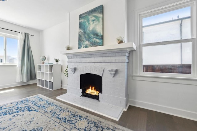 living room featuring a healthy amount of sunlight, dark hardwood / wood-style floors, and a brick fireplace