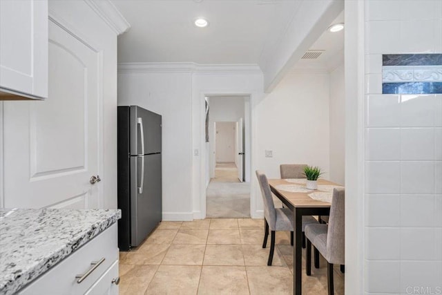 kitchen with white cabinetry, stainless steel fridge, light tile patterned floors, light stone counters, and crown molding