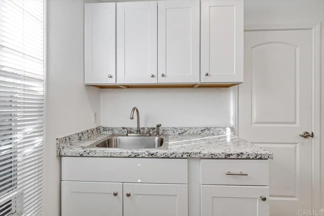 kitchen featuring sink, light stone countertops, and white cabinets