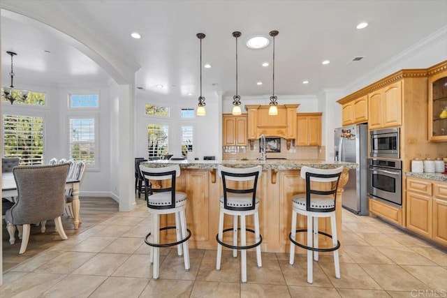 kitchen with light stone counters, appliances with stainless steel finishes, decorative light fixtures, and a kitchen island with sink