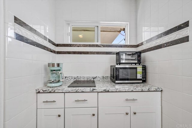 kitchen featuring light stone countertops, tile walls, and white cabinets