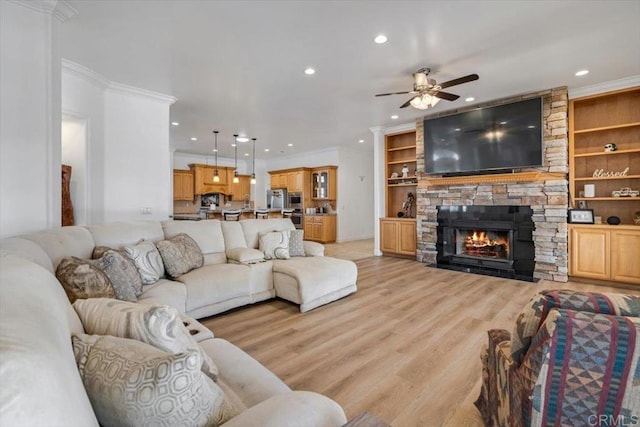 living room featuring built in shelves, light hardwood / wood-style flooring, ornamental molding, ceiling fan, and a fireplace