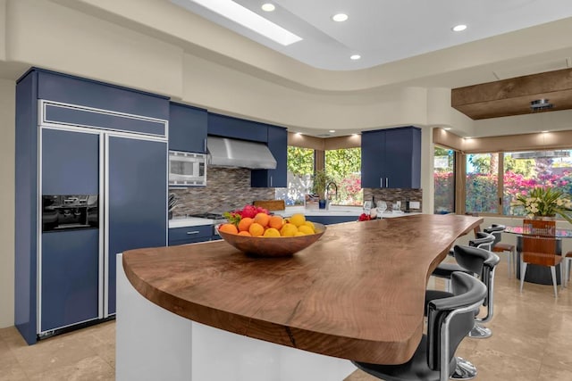 kitchen with blue cabinets, built in appliances, a skylight, decorative backsplash, and exhaust hood