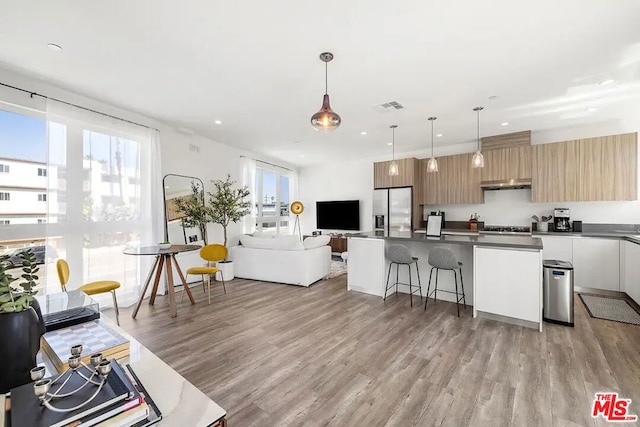 kitchen featuring a breakfast bar area, stainless steel fridge, light wood-type flooring, and decorative light fixtures