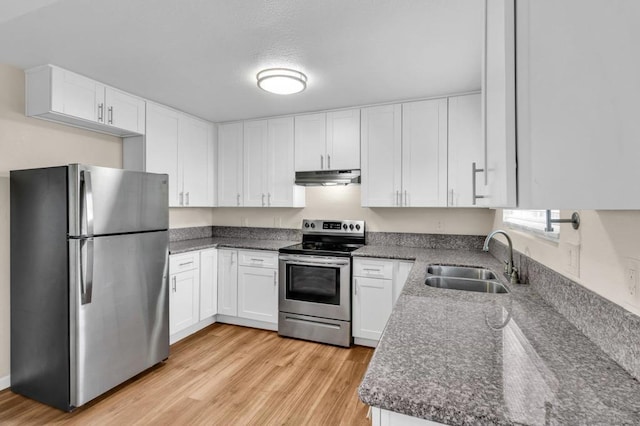 kitchen featuring sink, appliances with stainless steel finishes, white cabinetry, dark stone countertops, and light hardwood / wood-style floors