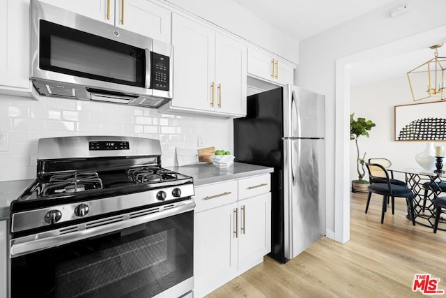 kitchen featuring appliances with stainless steel finishes, white cabinetry, hanging light fixtures, light hardwood / wood-style floors, and decorative backsplash