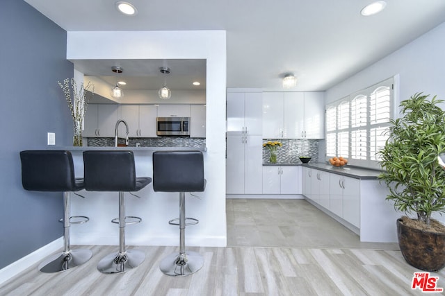 kitchen featuring a kitchen bar, white cabinetry, hanging light fixtures, kitchen peninsula, and decorative backsplash