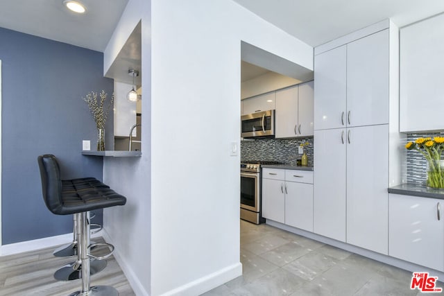 kitchen with white cabinetry, pendant lighting, stainless steel appliances, and decorative backsplash